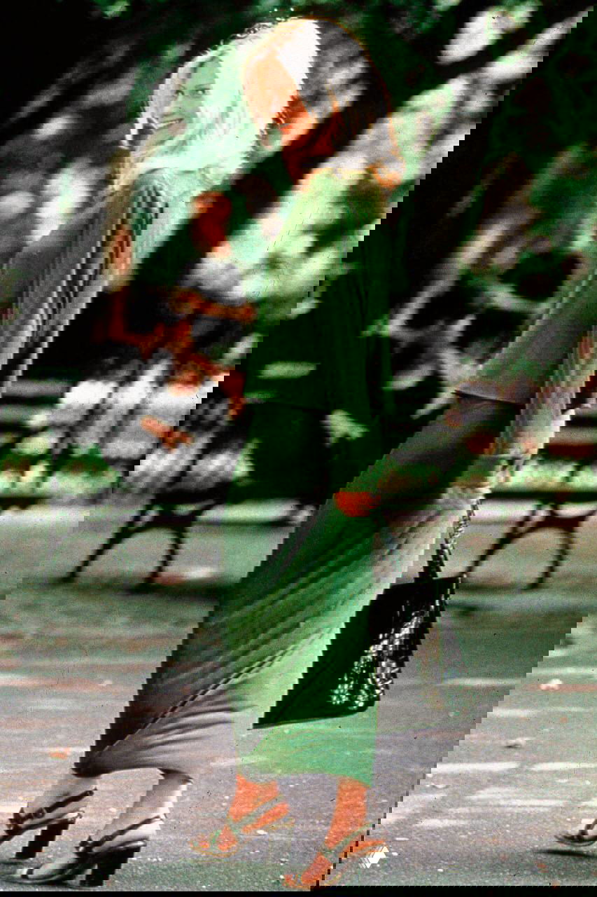 Ещё один архивный кадр в парковой зоне: световое пятно на волосах актрисы, зелёная юбка и сумка в руках, спокойная композиция.