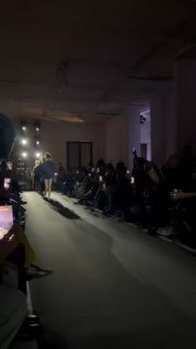 Панорамный кадр подиума Vesper Tverskaya: модели идут между зрителями при тусклом свете и включенных экранах телефонов.