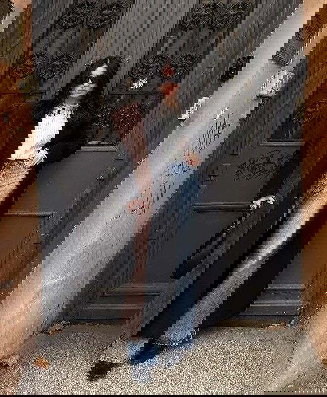 Стритстайл: женщина в длинном тёмном пальто с меховой вставкой и чёрным шарфом, образ в casual-стиле с широкими джинсами на фоне дверей.