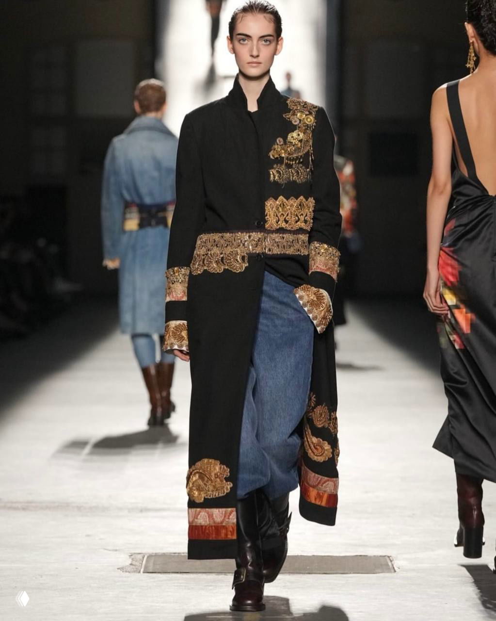 Модель в длинном чёрном пальто с золотыми барочными вставками и джинсами — сочетание текстур и ручной отделки в коллекции Dries Van Noten.