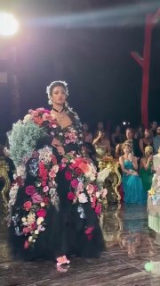 Модель в чёрном корсетном платье, украшенном пышными живыми цветами и жемчугом, шагает по подиуму Alta Moda в Таормине ночью