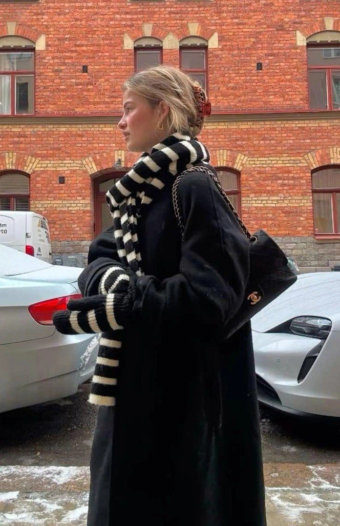 Профиль девушки в полосатом вязаном шарфе и перчатках на фоне кирпичной стены; образ с акцентом на полосатый принт и текстуру.