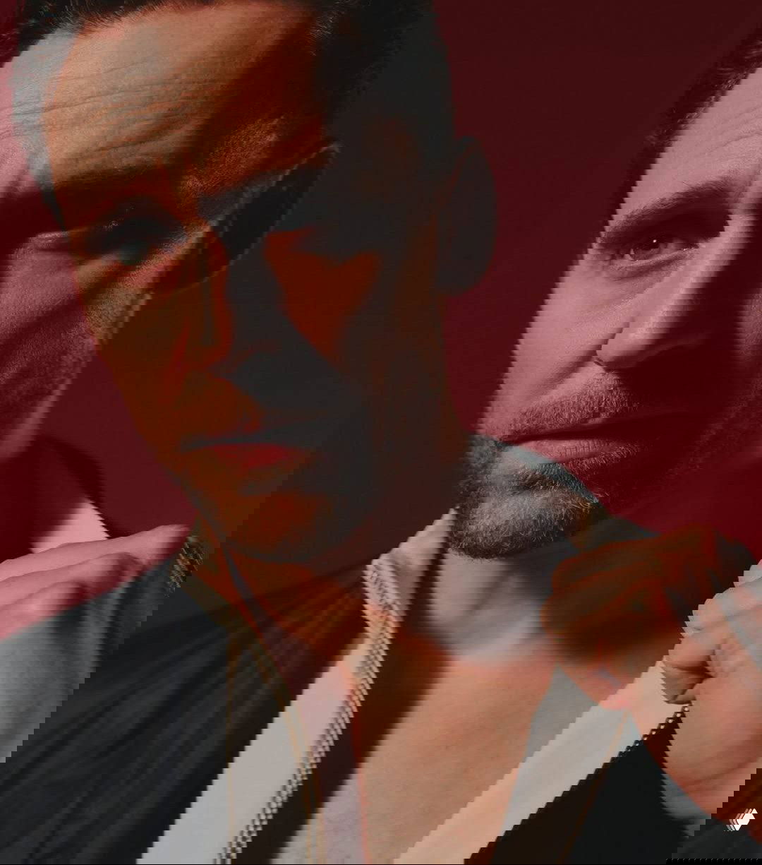 Крупный план мужчины-актера в студии на красном фоне — выразительный взгляд, фактурная кожа и контрастное освещение в портрете.