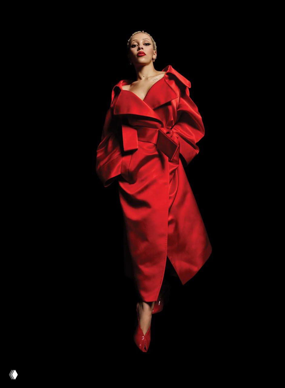 Доджа Кэт в длинном ярко‑красном платье на чёрном фоне — элегантный и театральный образ в студийной съёмке для Vogue, акцент на силуэте и цвете.