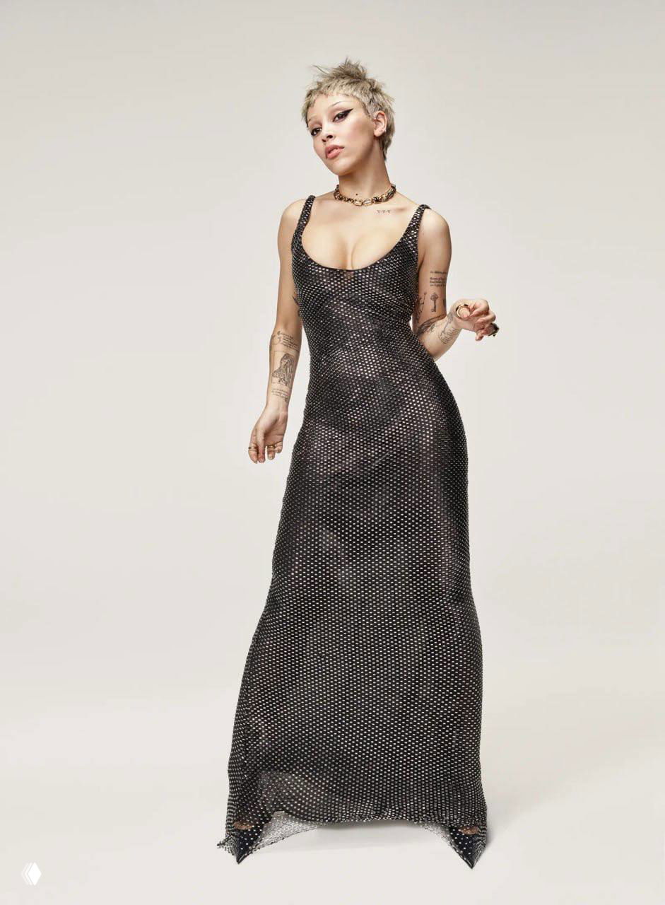 Доджа Кэт в облегающем длинном блестящем платье на нейтральном фоне — минималистичная студийная фотография, подчёркивающая силуэт и украшения.