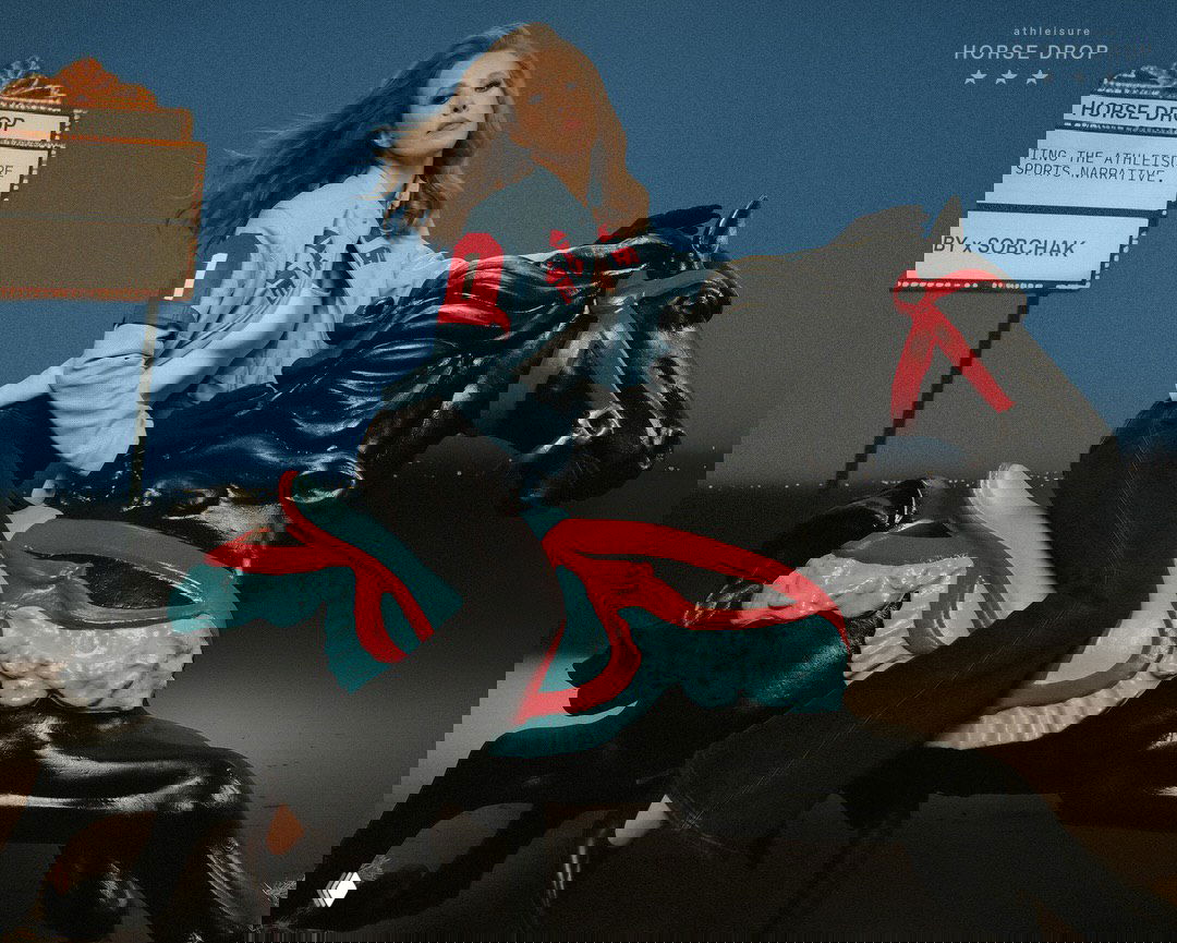 Женщина верхом на чёрной декоративной лошади в голубой укороченной куртке и джинсах — рекламный кадр коллекции IRNBY под названием «Horse Drop».