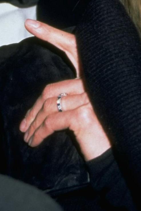 Крупный план руки с помолвочным кольцом: платиновое изделие, инкрустированное сапфирами и бриллиантами, видна фактура металла и огранка камней.