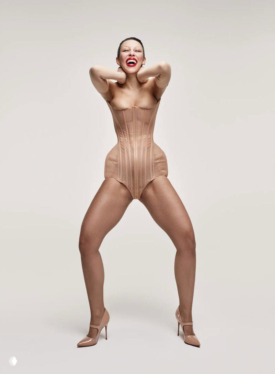 Доджа Кэт в нюдовом корсете и чулках на светлом фоне — игривый и театральный образ в студийной серии для апрельского номера Vogue.