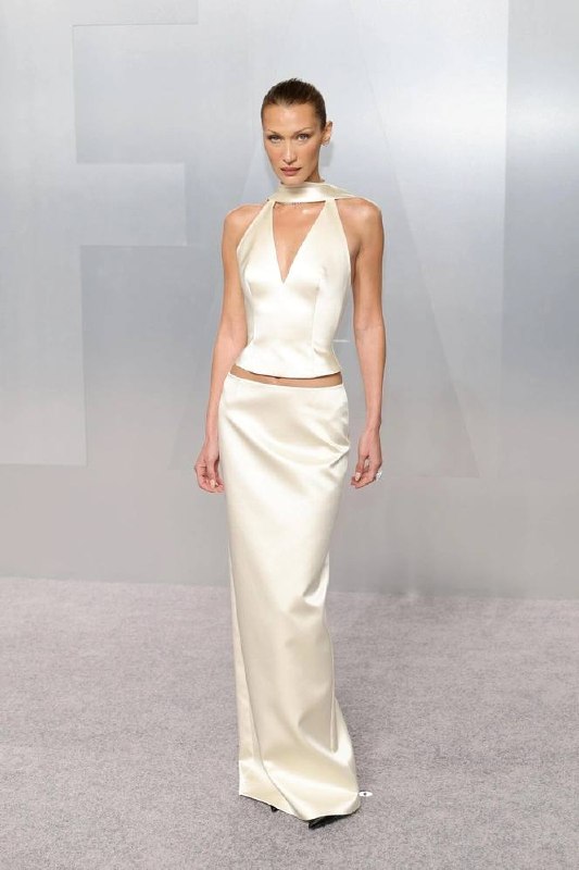 Высокая модель в шёлковом молочном платье прямого силуэта с вырезом, подчёркивающем строгую и элегантную линию для торжественного выхода.