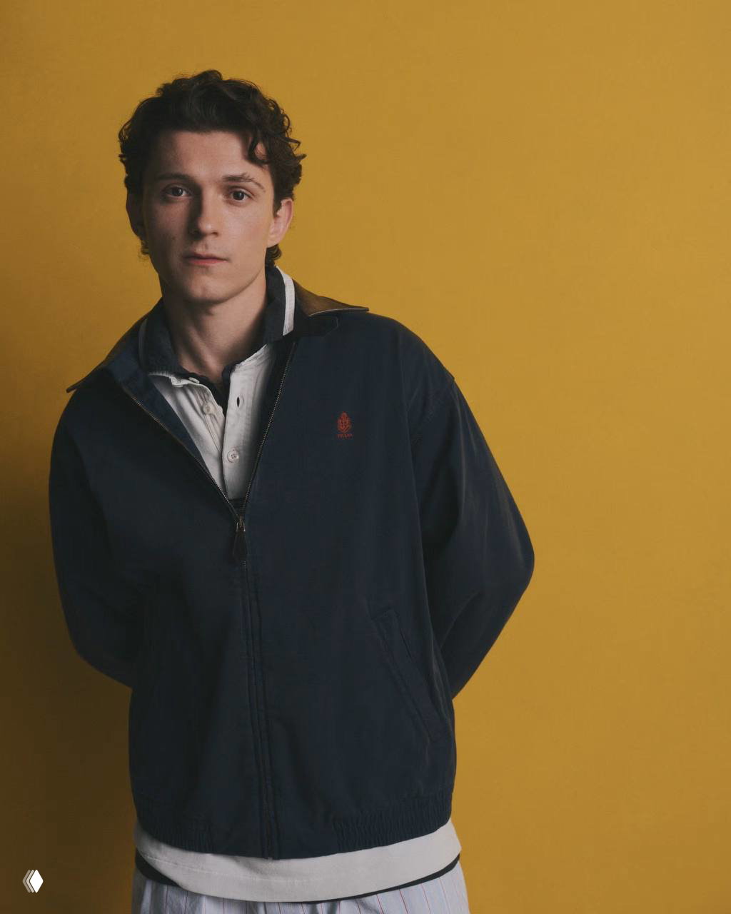Том Холланд в более повседневном образе на жёлтом фоне — полный рост в жакете и рубашке, студийная стилизация под модную съёмку.