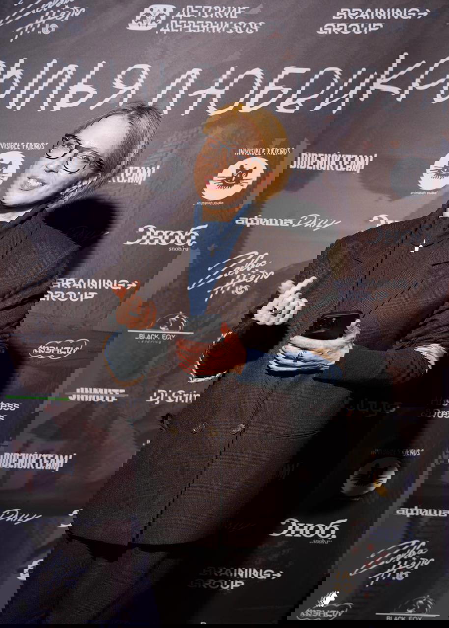 Гость премьеры позирует в фотозоне презентации анимационного фильма «Крылья любви» на фоне баннера с логотипами партнёров и названием проекта.