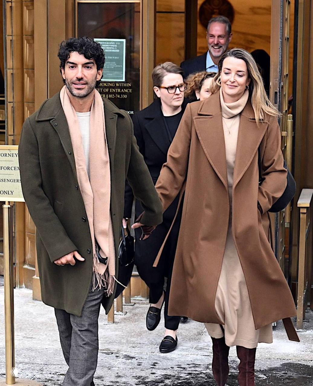 Пара идёт по заснеженной дорожке вне здания суда: мужчина в тёмном пальто держит за руку женщину в бежевом пальто, кадр папарацци.