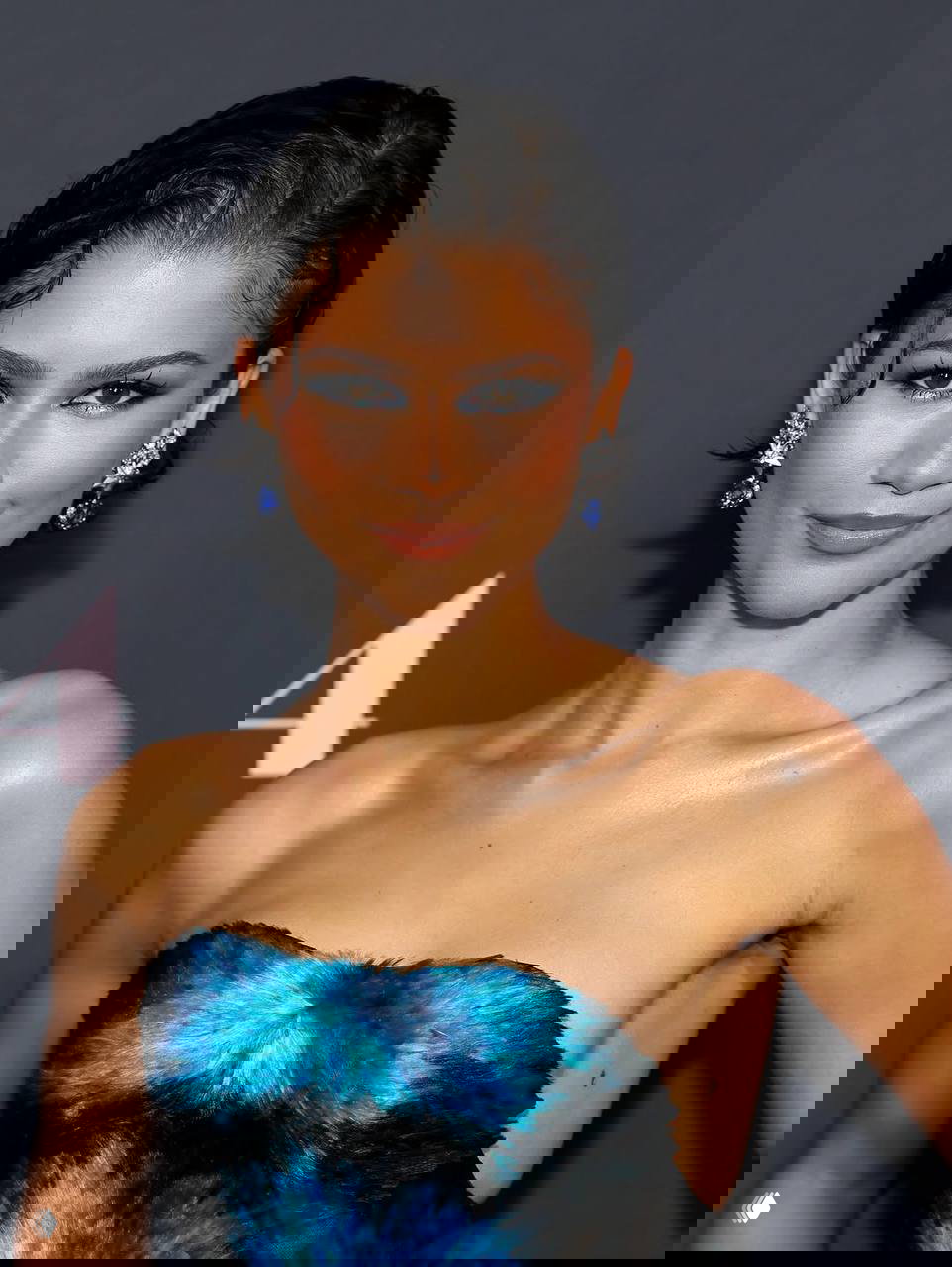 Крупный план лица и верхней части корсета с голубыми перьями; выражение лица и ювелирные серьги создают гламурный образ.