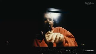 Крупный план сцены и экранов Coachella с исполнителем: зал подсвечен, артист близко к камере, зрительские экраны видны внизу.