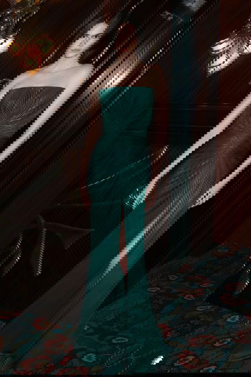 Фотография образца платья в студийной обстановке — модель в изумрудном платье на фоне тёмной обстановки, демонстрация кроя и ткани.