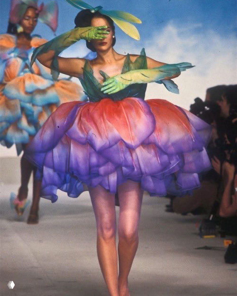 Главная модель в пышном платье‑цветке Mugler с градиентной окраской от пурпурного к фиолетовому, декоративные перчатки и театральный показ.