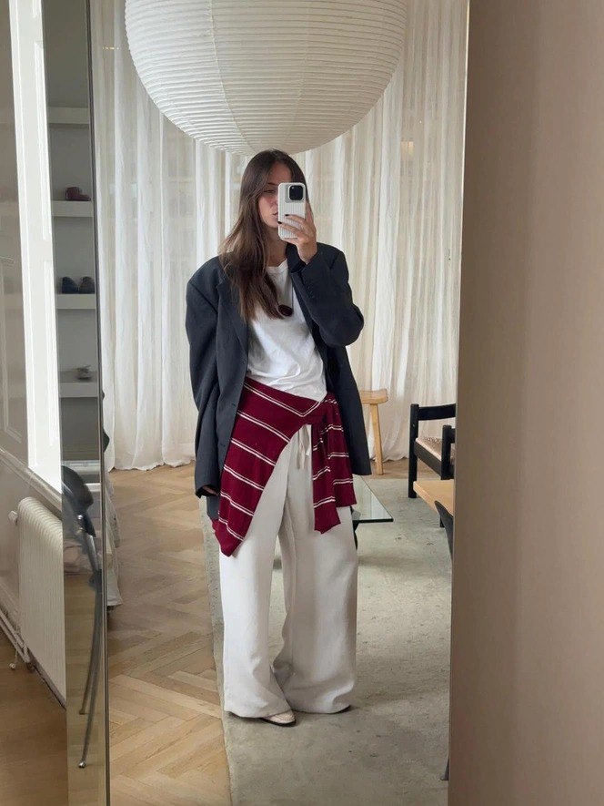 Селфи в зеркале: широкие белые брюки в сочетании с белой футболкой и тёмным оверсайз‑пиджаком, светлая комната с крупной подвесной лампой на фоне.