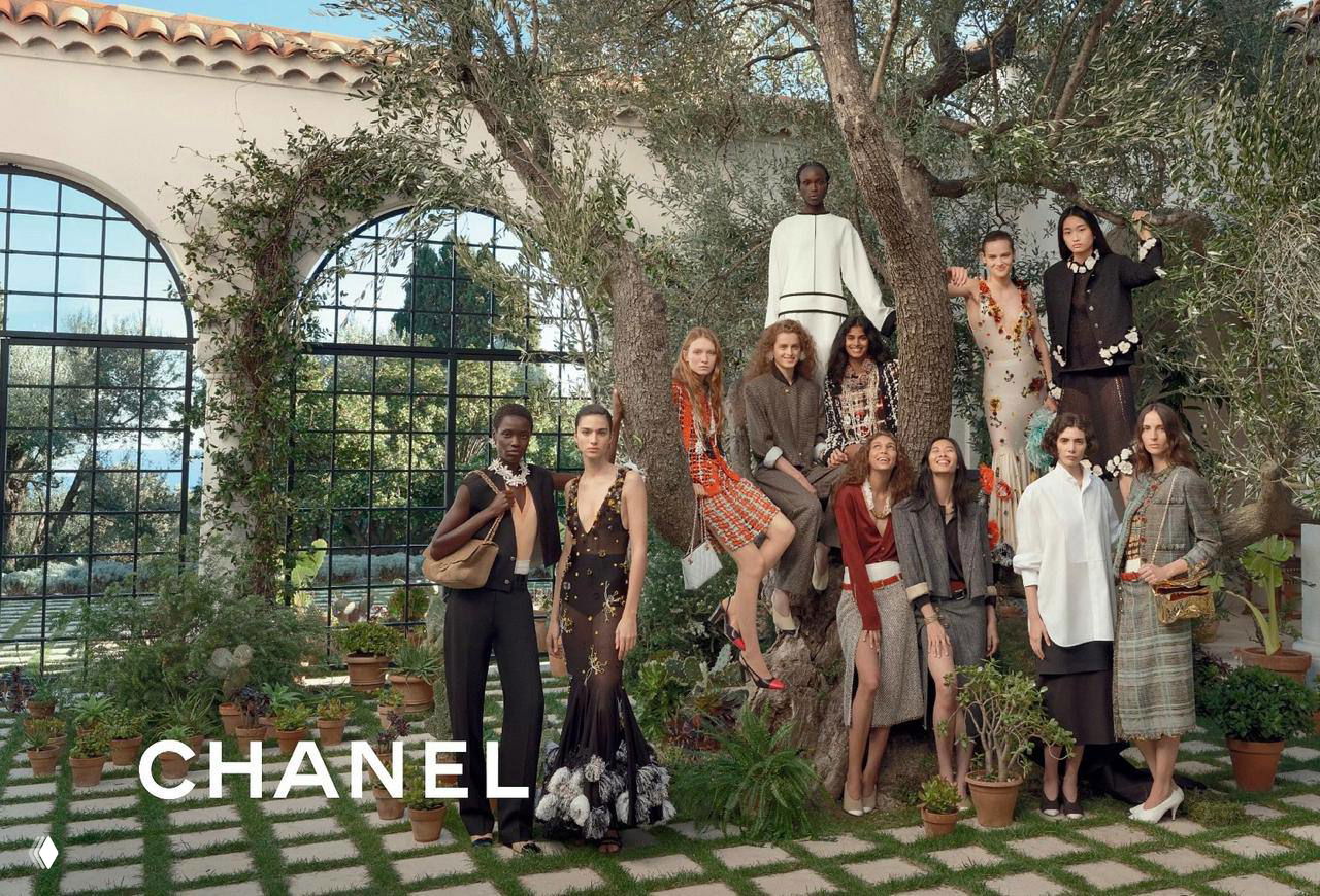 Групповой кадр кампейна Chanel: несколько моделей в нарядах коллекции на открытой террасе среди зелёных растений, логотип CHANEL внизу кадра.