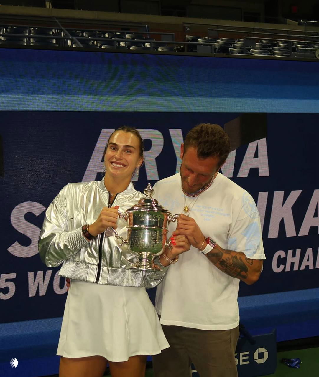 Арина держит трофей Уильямс Оупен рядом с Георгиосом Франгулисом, пара улыбаясь позирует на корте после победы и вручения кубка.