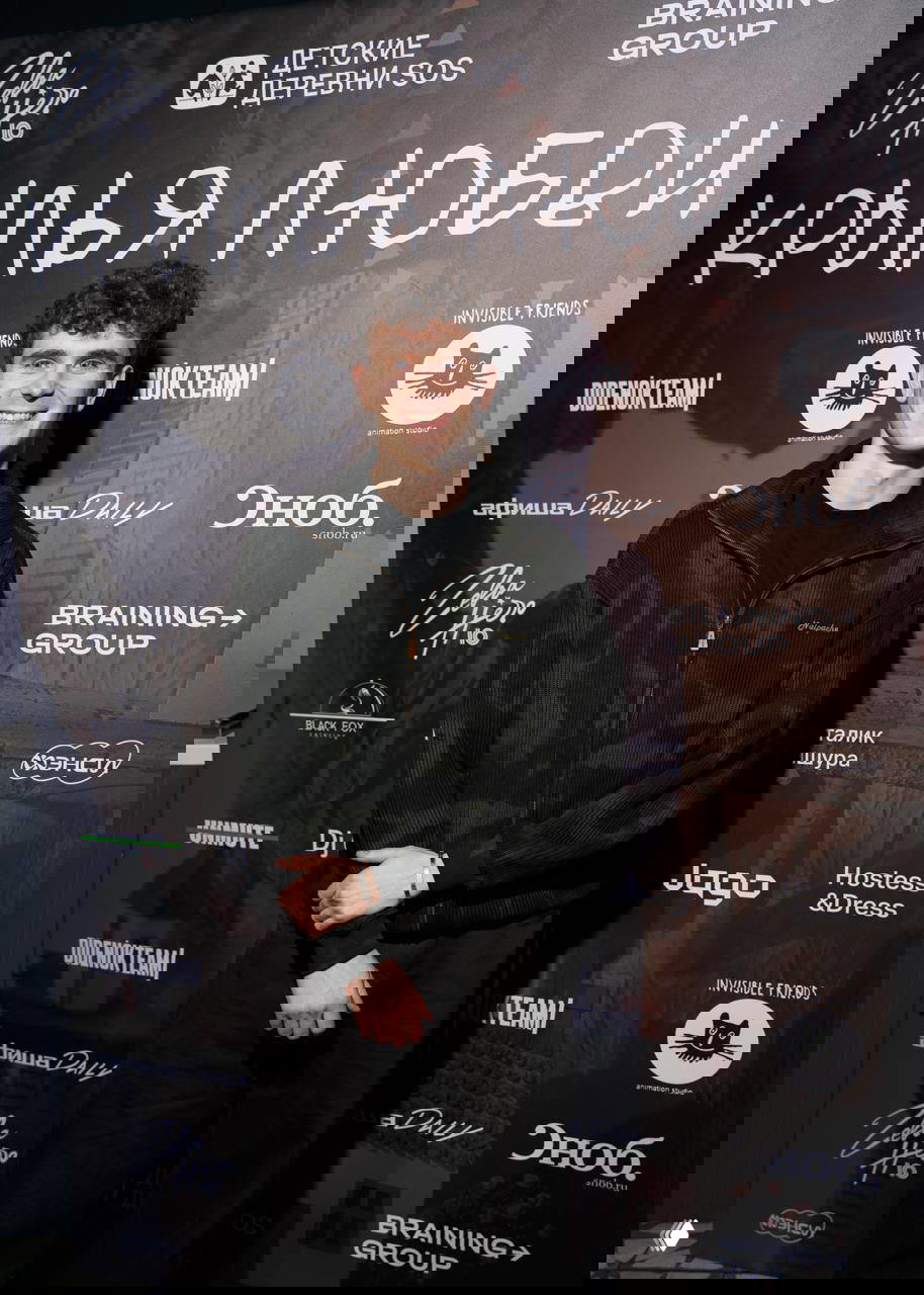 Молодой гость улыбается на фоне баннера с надписью «Крылья любви» и логотипами организаторов и партнёров мероприятия в Москве.