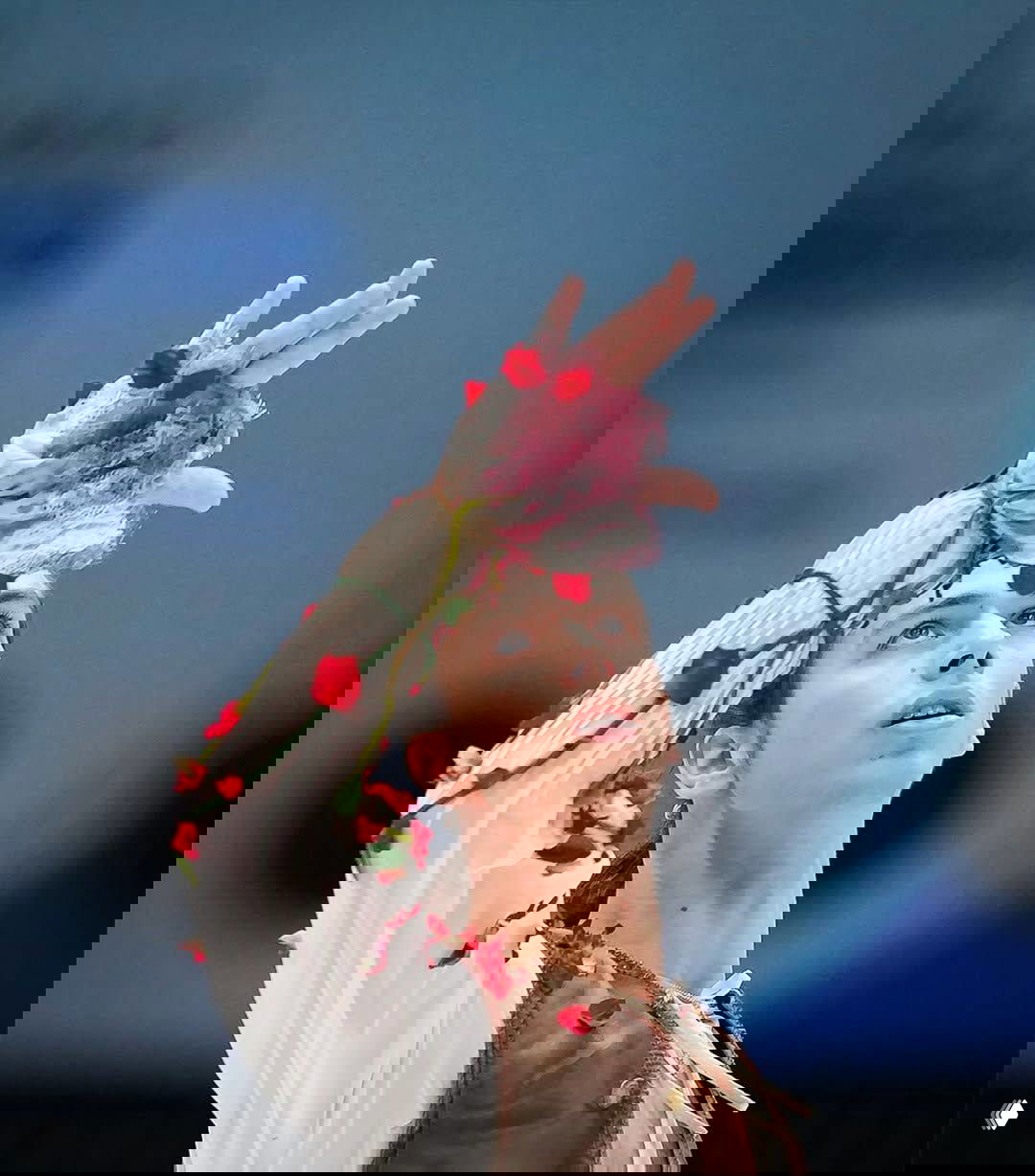 Крупный план руки и лица фигуриста в блузе с пришитыми розами и кружевом, кадр из короткой программы на соревновании.