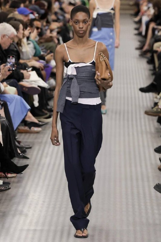 Модель в строгих брюках и асимметричном топе, с сумкой на показе — элегантный образ, который перекликается с тенденциями Saint Laurent.