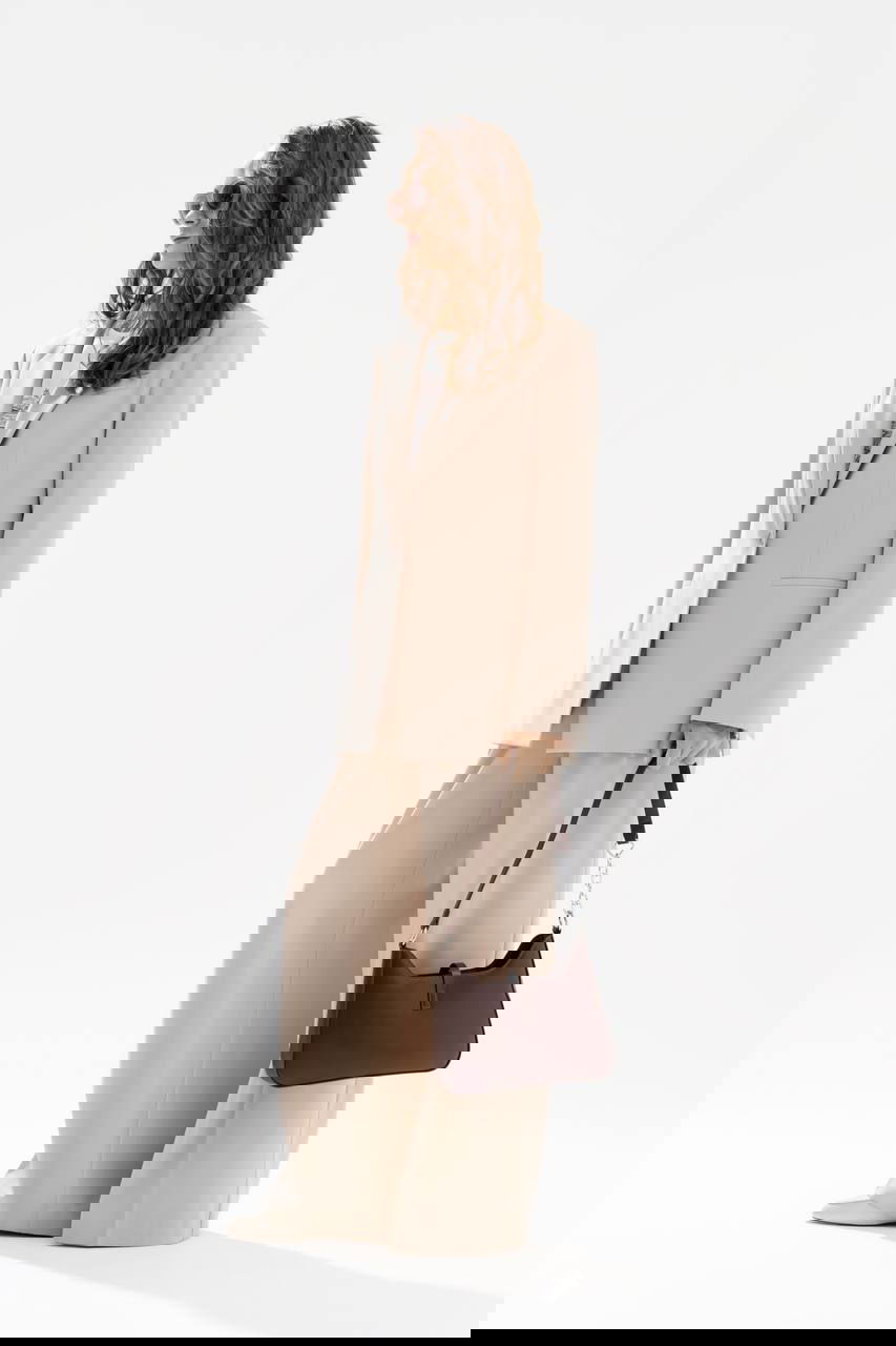 Фотография коллекции Nelva: модель в бежевом жакете и широких брюках с коричневой сумкой на светлом фоне — минималистичный деловой стиль.