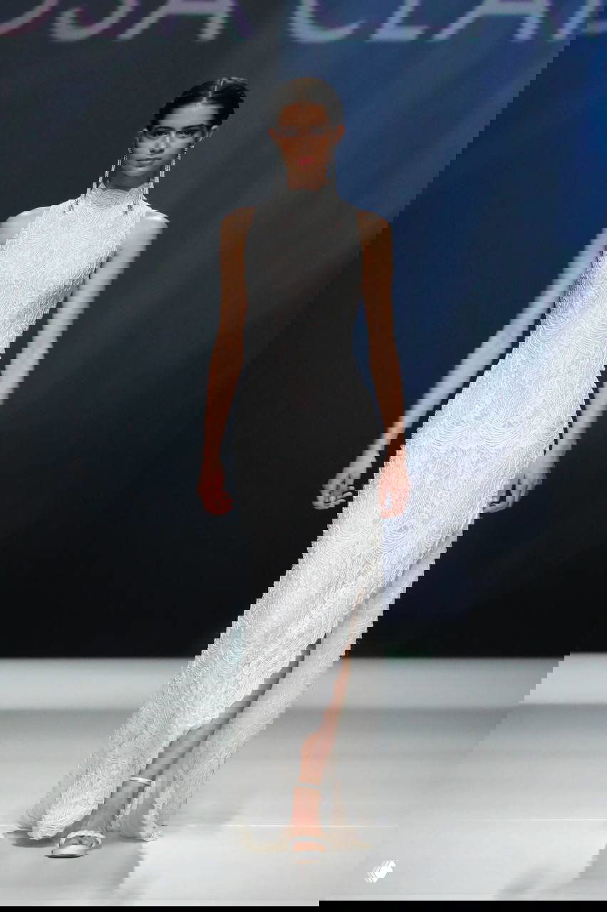 Модель в облегающем кружевном платье с высоким воротником и изящным разрезом; кружево создаёт графичную текстуру на показе.