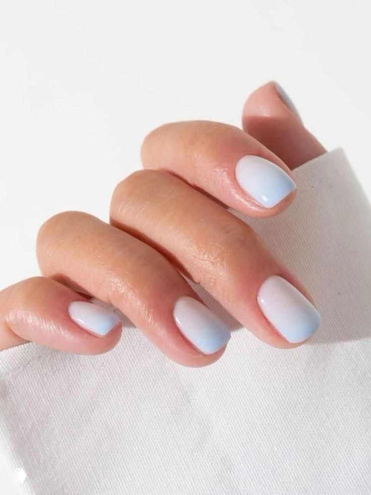 Крупный план руки с гладким бледно-голубым омбре-маникюром на аккуратных коротких ногтях, нейтральный фон и мягкое освещение.