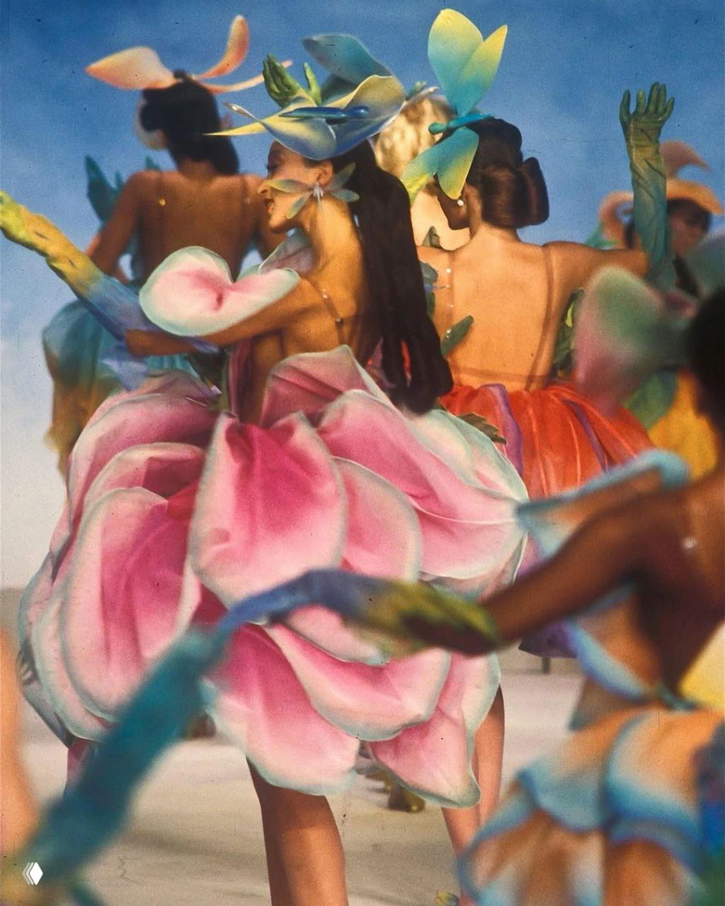 Групповая сцена показа Mugler 1982: несколько моделей в платьях‑цветах, акцент на объёмных лепестках и хореографию подиумного дефиле.