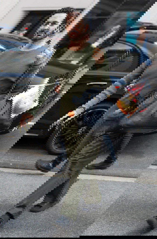 Мужчина в повседневной одежде идёт по улице; у сумки видна упаковка или брелок с игрушкой Labubu — уличный стрит‑кадр с акцентом на аксессуар.