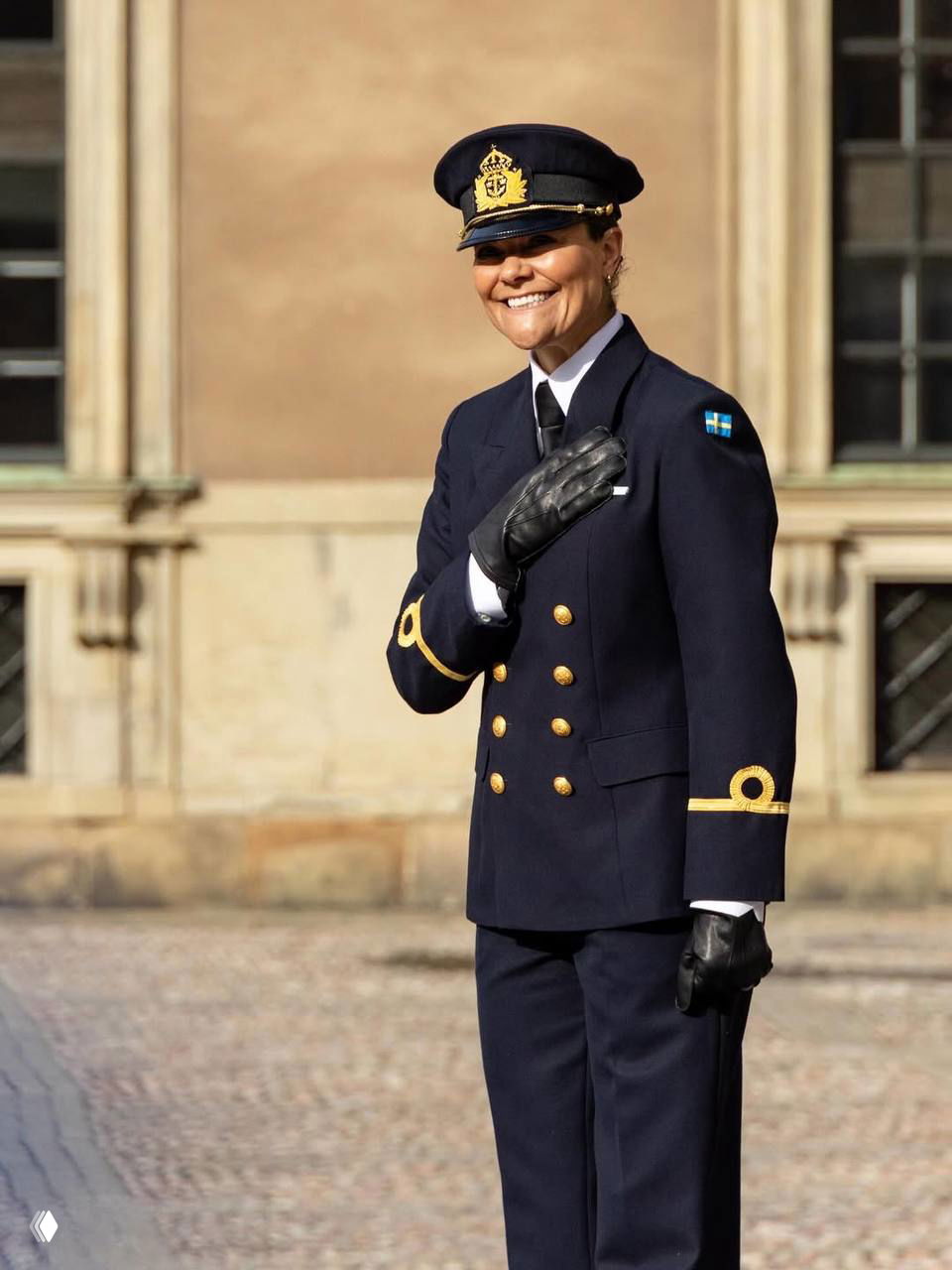 Наследная принцесса Виктория улыбается на публике в парадной форме, рука у груди, солнечное освещение подчёркивает тёплую атмосферу праздника.