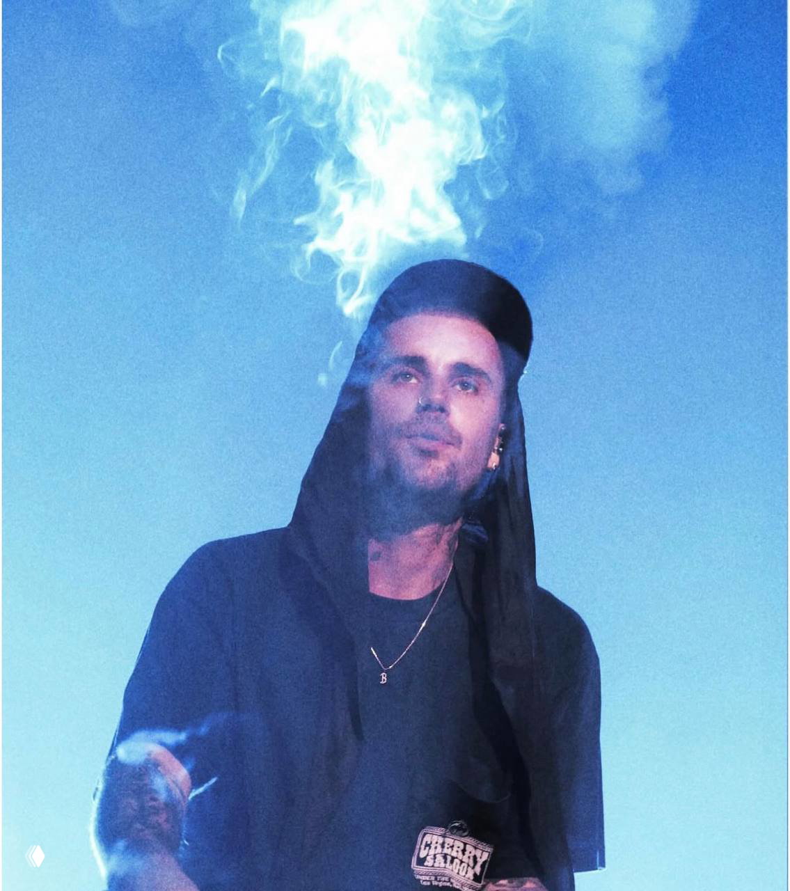 Джастин Бибер на сцене Coachella: певец в худи и кепке под эффектным дымом и синим подсветом, кадр сценического выступления.