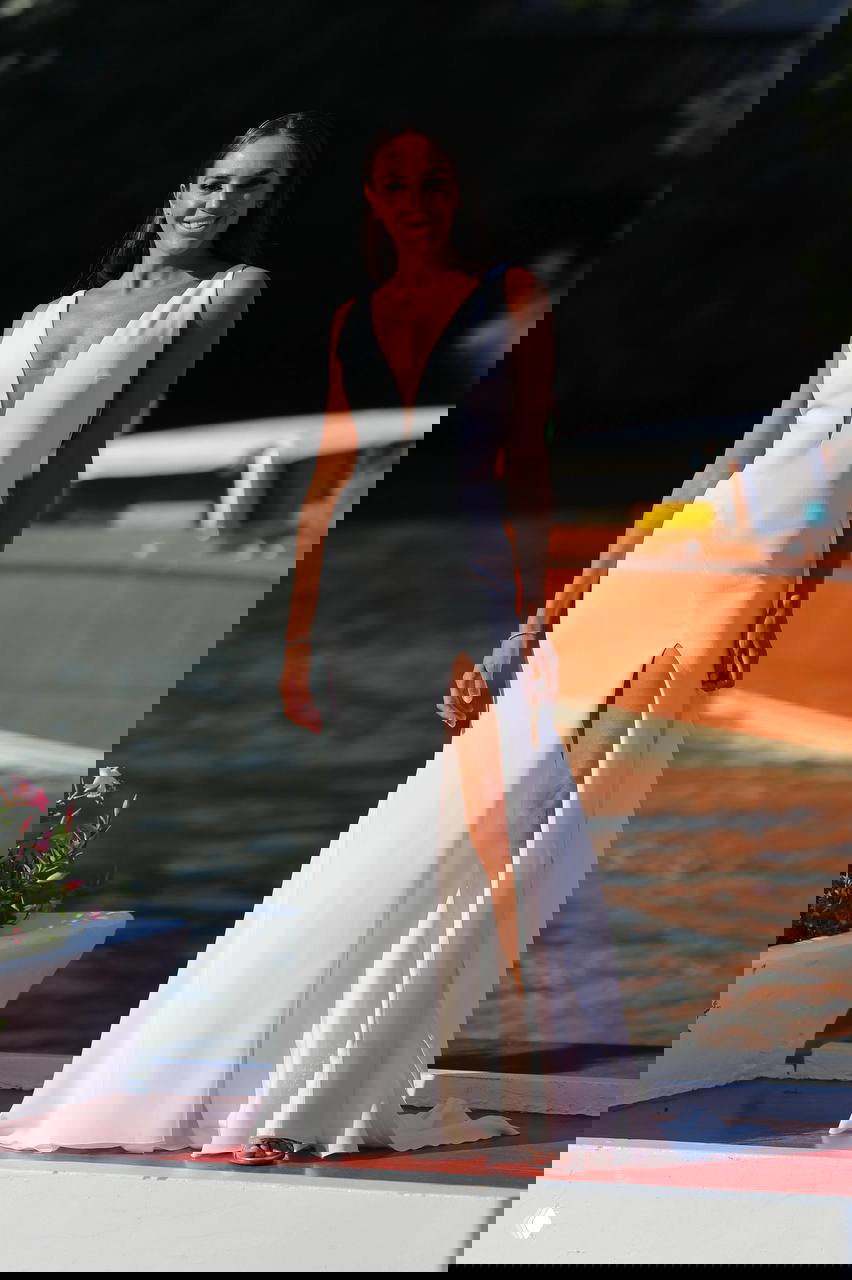 Модель на набережной в платье с глубоким разрезом и декольте; на фоне видна вода и прогулочная лодка, образ выездной церемонии.