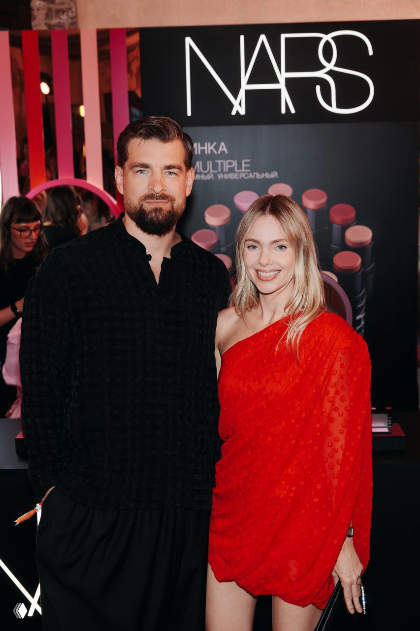 Посетители у стенда NARS: пара позирует на фоне выставки средств макияжа NARS на Marie Claire Blogger Party 2026, видны логотипы и продукты бренда.