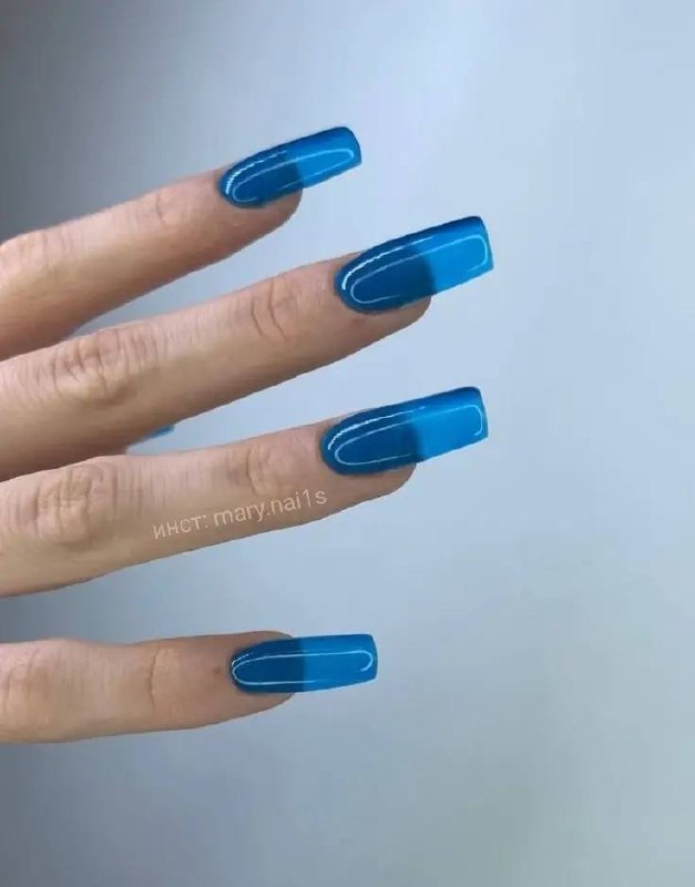 Рука с синим «стеклянным» маникюром на удлинённых квадратных типсах: яркий синий оттенок с эффектом прозрачного стекла на кончиках.