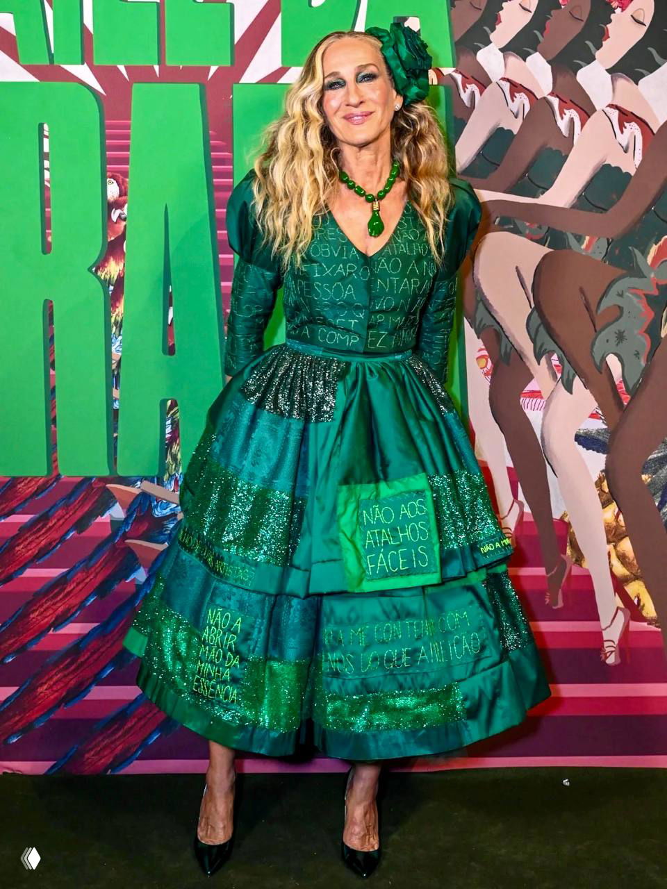 Сара Джессика Паркер на фоне яркой фотозоны Baile da Arara в Рио; видны детали вышивки на платье и эффектные зелёные украшения.