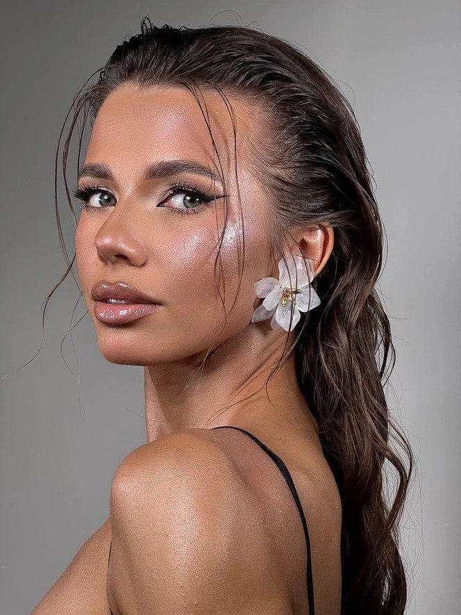 Брюнетка с эффектом мокрых волос и подчёркнутым свечением кожи, выразительной чёткой стрелкой на глазах и акцентом на текстуре лица