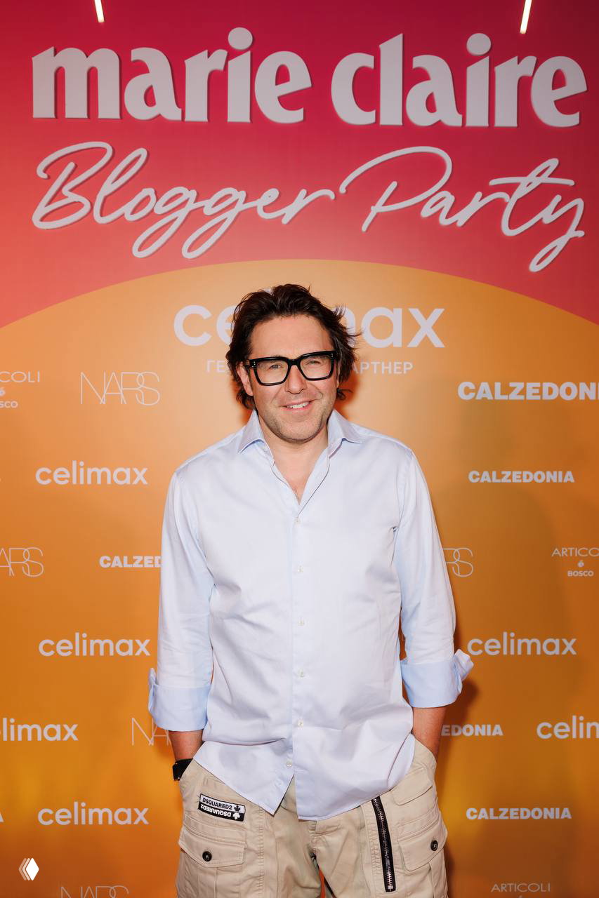 Гость у бренд-волла Marie Claire Blogger Party 2026: оранжево-розовый бэкстейдж с логотипами партнёров и праздничной атмосферой для фото гостей.