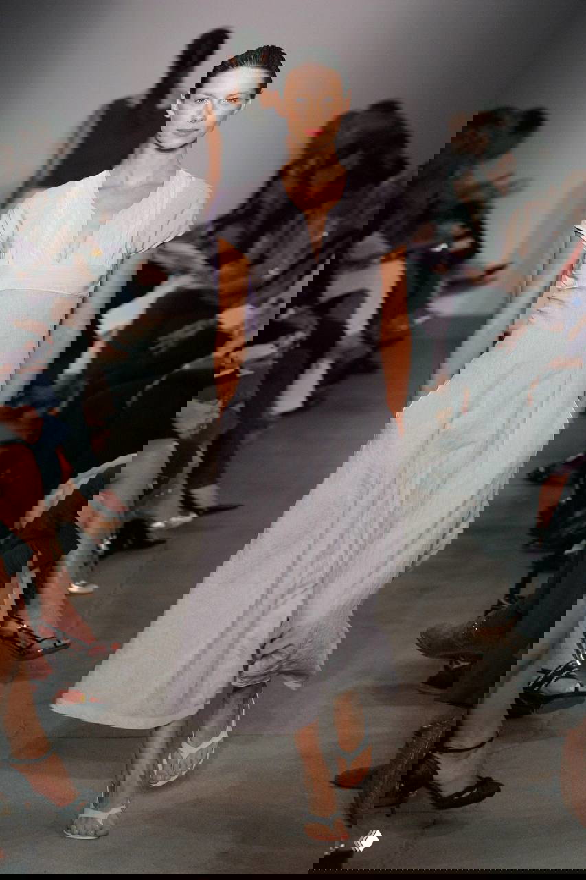 Показ мод: женщина в льняном свободном платье светло-серого оттенка, минималистичный крой и аккуратная простота на подиуме.