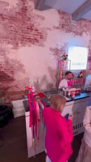 Бар Schmidt внутри помещения Blogger Party: стойка с брендингом, бармены в розовой униформе и гости у стойки в вечерней, летней обстановке.