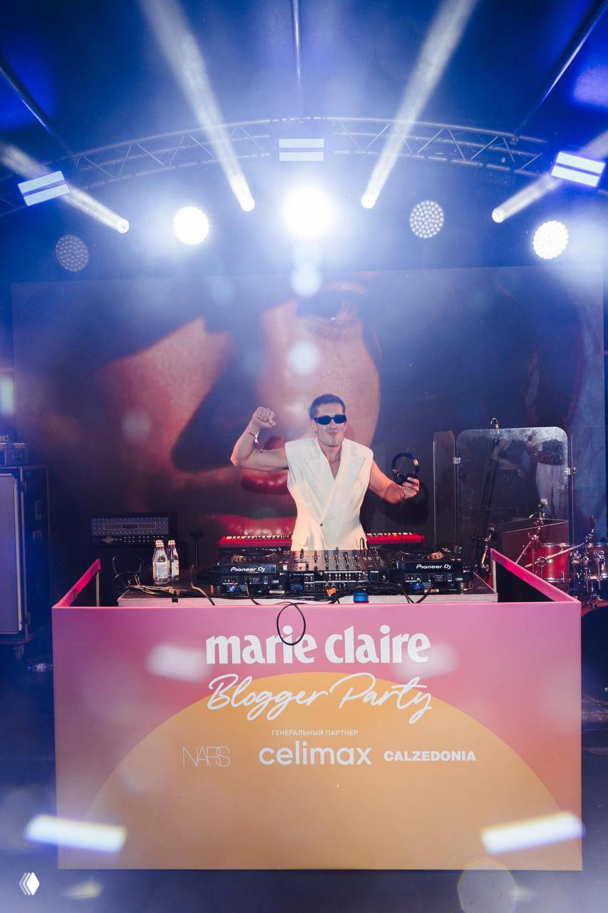 Диджей за пультом Marie Claire Blogger Party 2026: ночная сцена, сценические огни и брендинг мероприятия на переднем плане у диджейского стола.