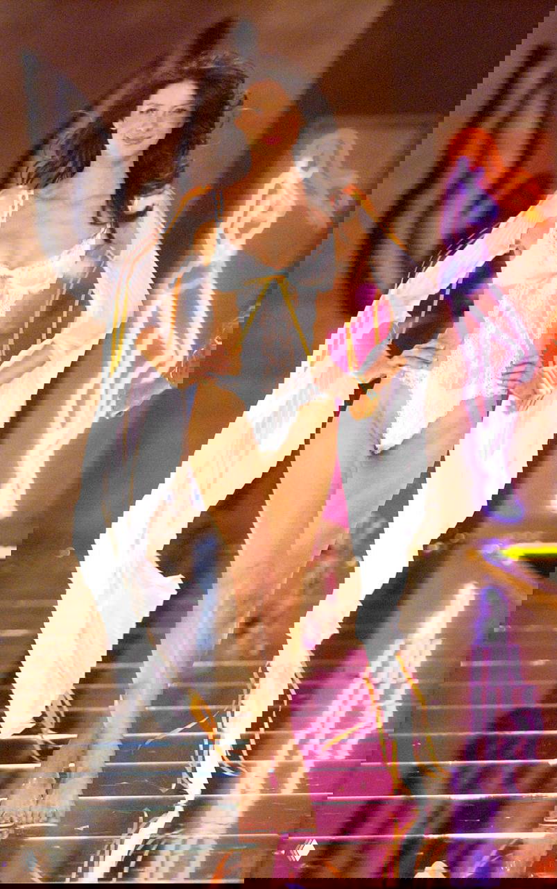 Сцена дефиле: женщина в кружевном нижнем белье и прозрачных элементах, визуальный фокус на формах и сценическом оформлении показа.