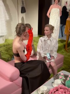 Гости и модели в вечерних нарядах беседуют на розовой мягкой мебели в фэшн-зоне; кадр атмосферы и общения во время показа в Москве.