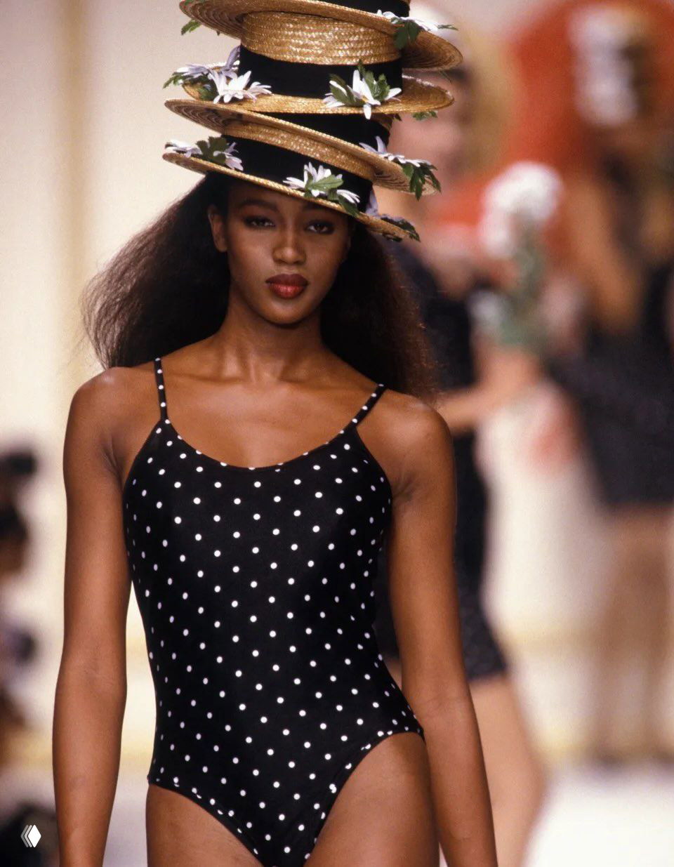 Модель в гороховом слитном купальнике идёт по подиуму в летнем образе; ретро-кадр с коллекции, акцент на аксессуарах.