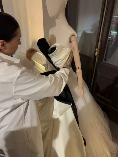 Дизайнер или ателье мастер аккуратно драпирует и примеряет ткань на манекене в белом халате — процесс подготовки к показу и примерки кутюрного платья.