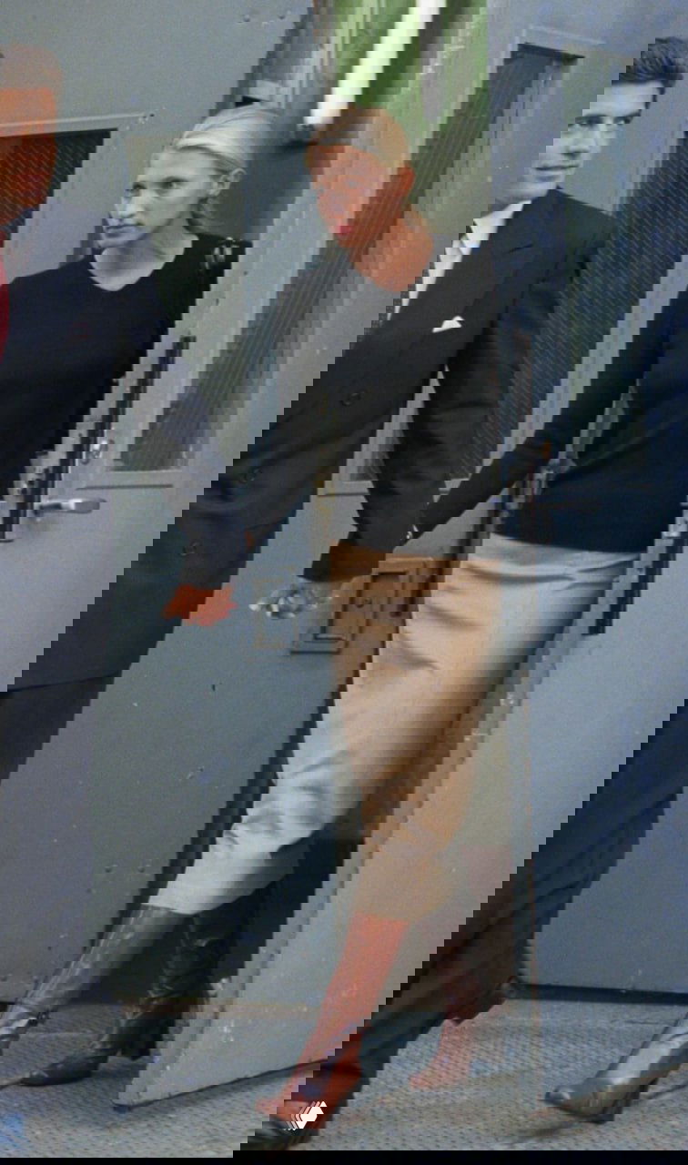 Женщина в чёрном топе и бежевой юбке с высокими коричневыми сапогами, уличный кадр в стиле 90‑х с подчёркнутым минимализмом.