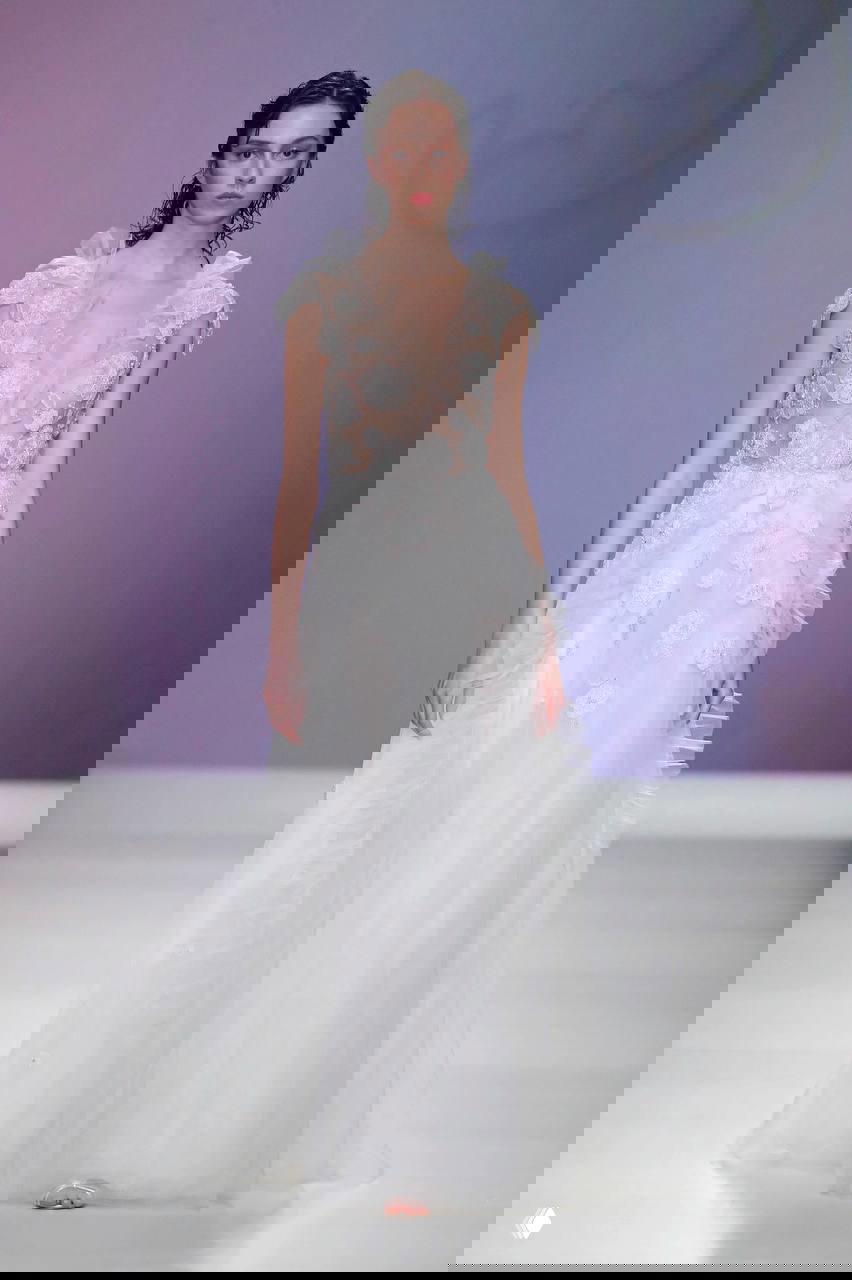 Модель на подиуме в прозрачном кружевном корсете с цветочными аппликациями и пышной тюлевой юбкой на светлом фоне показа.