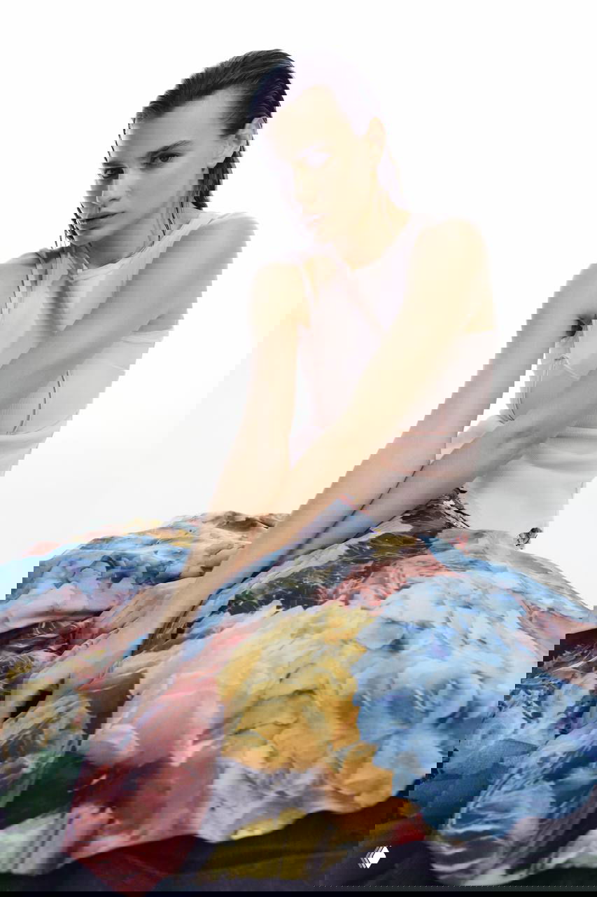 Сидящая модель Алина в платье с крупным цветочным принтом и пастельным топом на белом фоне — эстетика весны в съемке.