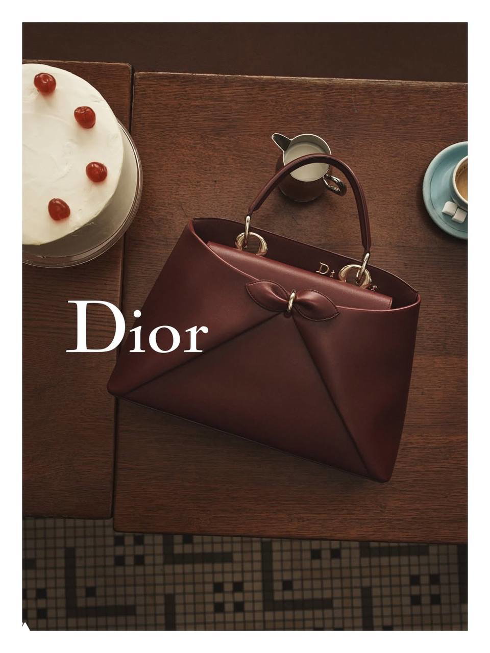 Вид сверху на коричневую сумку Dior рядом с тортом и чашкой кофе — натюрморт-кадр из кампании в кафе, стол, торт, кофейная чашка и текстуры дерева в кадре.